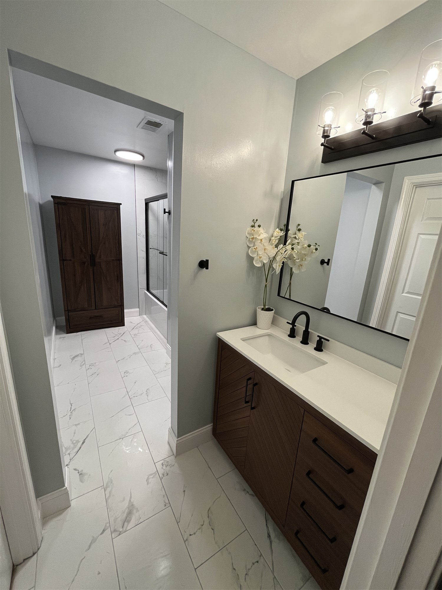 Completed bathroom with white tile, a dark vanity, and a glass shower enclosure.