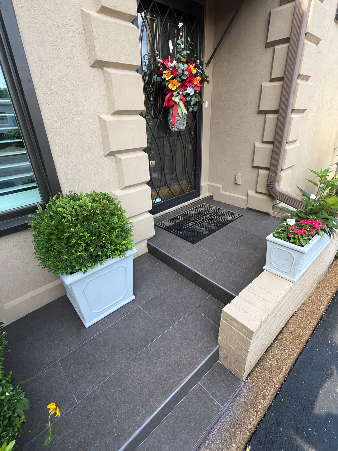 Completed dark tile entryway with a front door and planters.