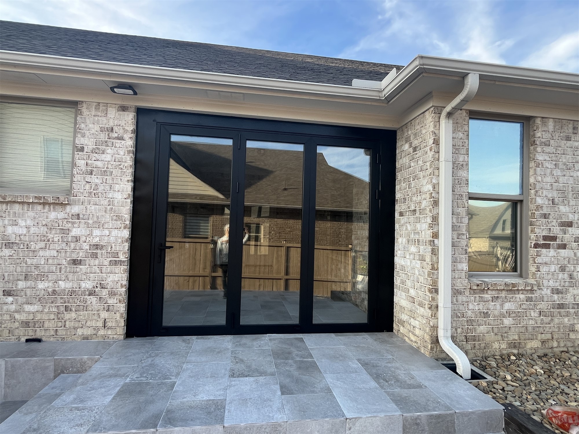 Completed covered entry with black-framed patio doors and light stone tile.